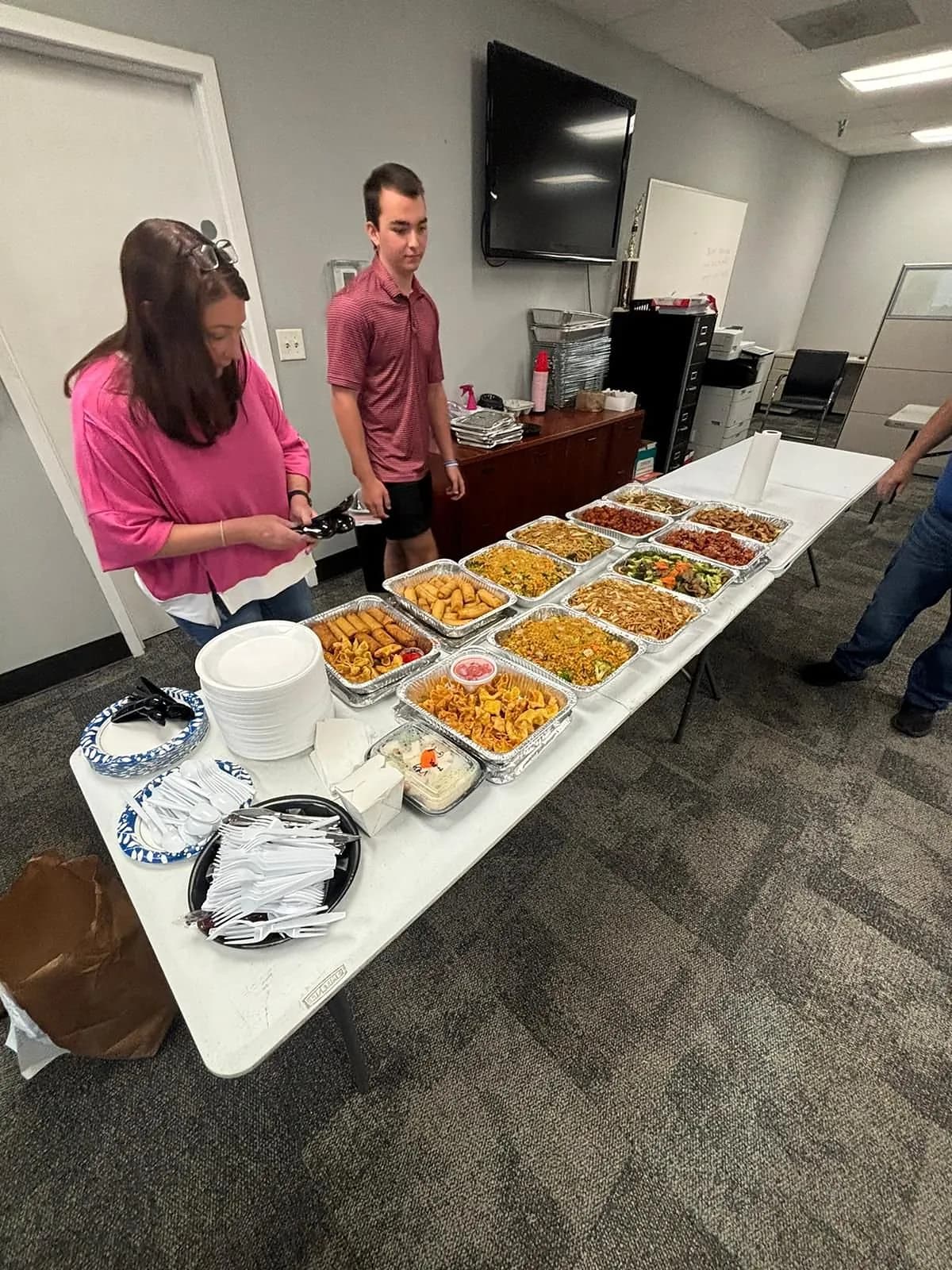 Two people at the end of a long office table set with catering trays, plates and napkins