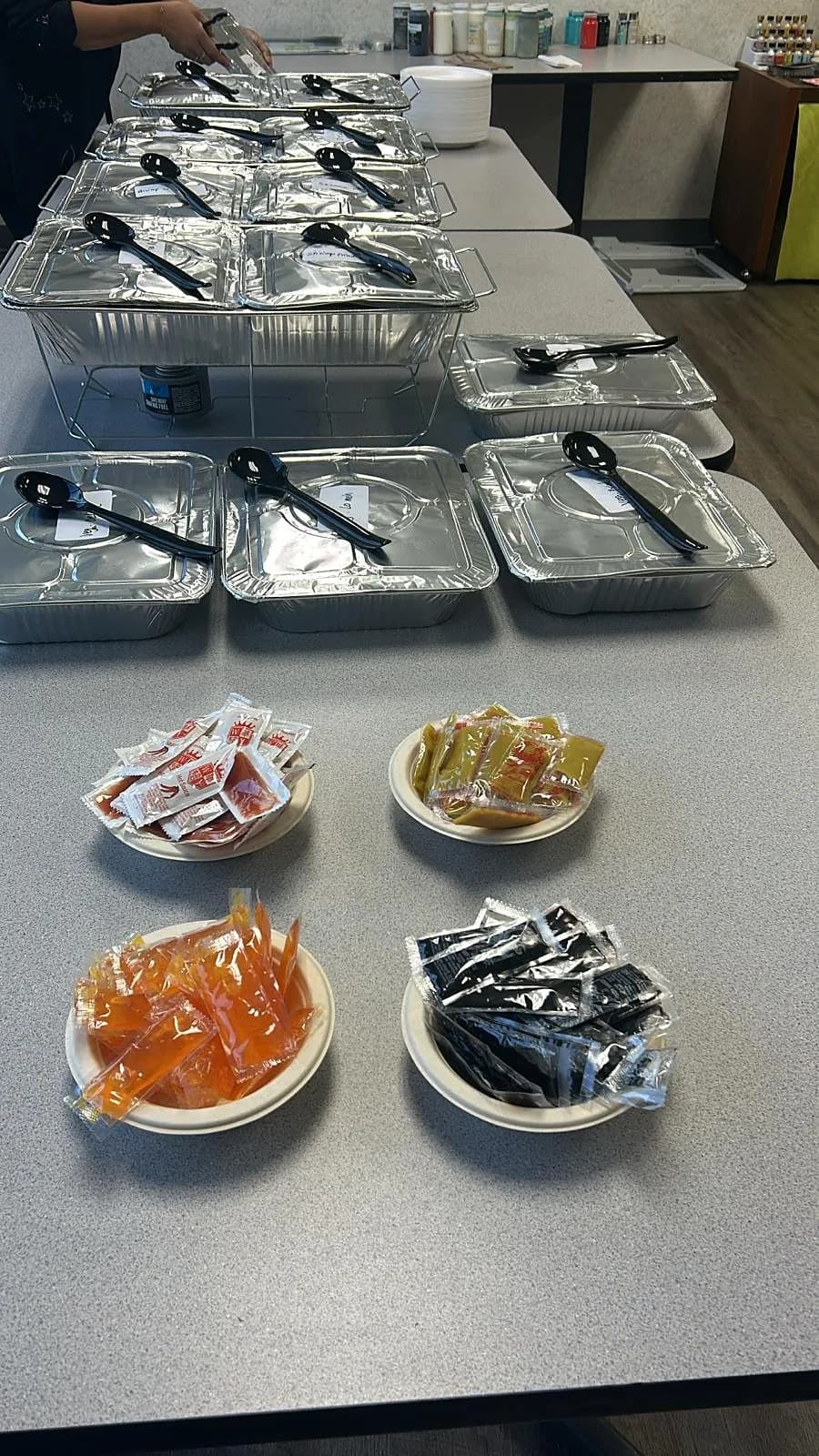 Foil catering trays with serving spoons and bowls of sauce packets set out on office tables