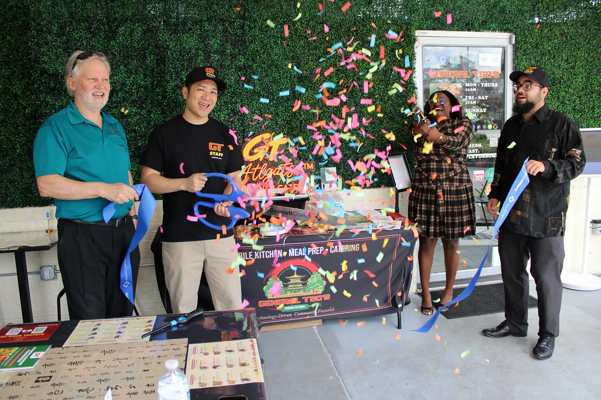 Confetti flies as Patrick Cheng and three guests cut a blue ribbon beside a General Tso's catering table