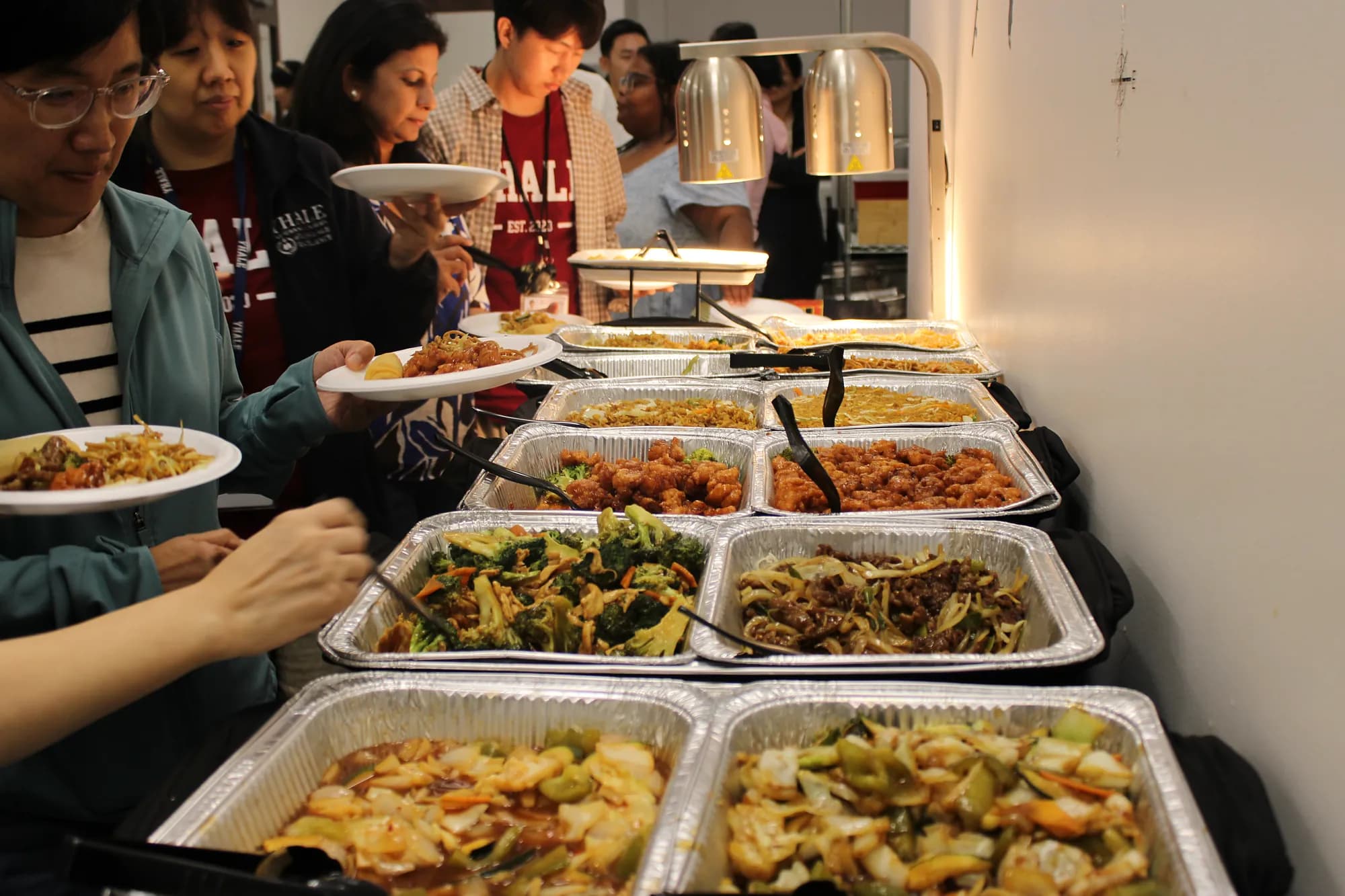 Guests in YHALE T-shirts fill their plates from trays of orange chicken, broccoli and stir-fried vegetables