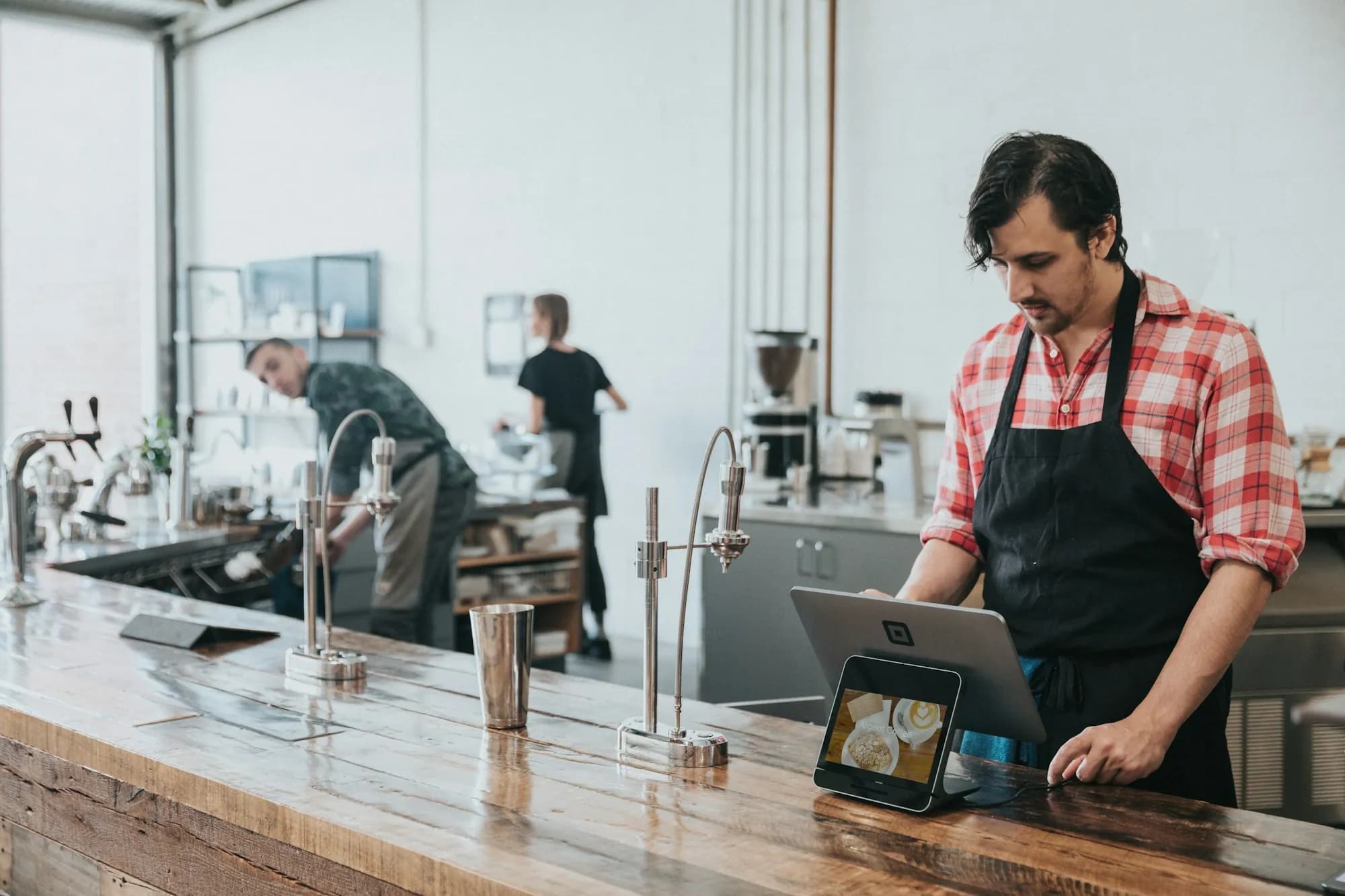 Cafe worker in an apron entering an order on a tablet register at a wooden counter